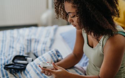 Young girl testing her blood sugar on a glucometer while sitting in bed. 