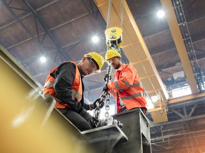 Steel workers fastening steel to crane in factory